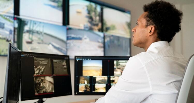 Young adult male security worker watching video wall while sitting at desk
